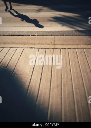 Ombra di persona il jogging in un crosswalk sul marciapiede. Foto Stock