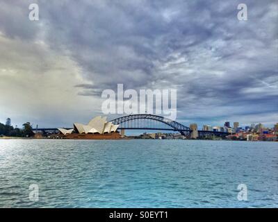 Il Ponte del Porto di Sydney e opera su una Domenica nuvoloso con le acque blu della baia Foto Stock