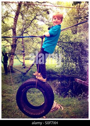 Ragazzo basculante in una corda e il pneumatico. Corso di avventura. Corso d'assalto. Giochi di bosco Foto Stock