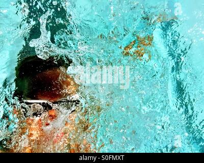 Primo piano sopra l uomo nuoto concorrenza dorso in una piscina esterna. Sun luccicante attraverso la riattivazione e spruzzi d'acqua. Foto Stock