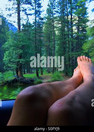 Un giovane adulto si rilassa con i suoi piedi fuori dalla finestra mentre ammirate Merced Creek Foto Stock