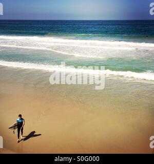 Un surfista maschio passeggiate fino alla spiaggia. Manhattan Beach, California. Stati Uniti d'America. Foto Stock