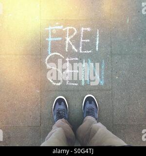 Un mans piedi piedi accanto alle parole "Frei Sein" (Libero) scritto sul marciapiede in tedesco con colorati chalk Foto Stock