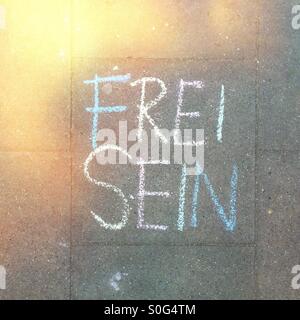 Le parole "Frei Sein" (Libero) scritto sul marciapiede in tedesco con colorati chalk Foto Stock