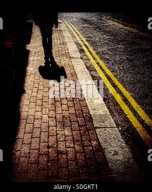 Uomo che cammina sulla strada con ombre lunghe Foto Stock