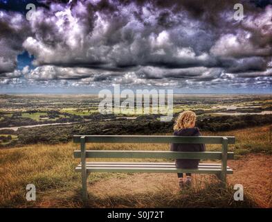 Ragazza giovane da solo su un banco di lavoro guardando avvicinando nuvole di tempesta Foto Stock