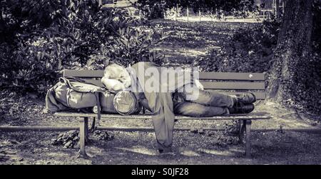 Senzatetto uomo dorme su una panchina nel parco Foto Stock