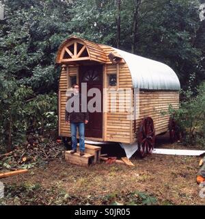 Pastori in legno stile capanna log cabin nei boschi con un uomo sui gradini, Hampshire, Emgland, Regno Unito. Foto Stock