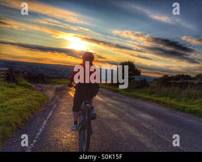 Escursioni in bicicletta verso il tramonto sulla strada di un paese a Otley Chevin West Yorkshire Foto Stock