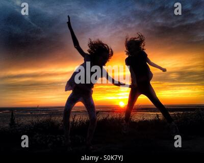 Bambini che si divertono in silhouette contro il sole di setting Foto Stock