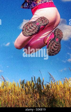 Le gambe della ragazza saltando sopra il campo di grano contro un cielo blu Foto Stock