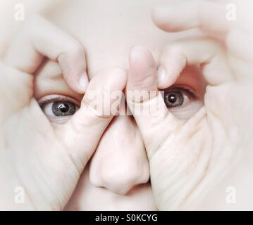 Ragazza giovane cerca attraverso occhiali realizzati dalla sua dita Foto Stock