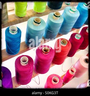 Colorato assortimento di bobine in filo da cucire organizzate per ombra in uno spazio di lavoro luminoso Foto Stock