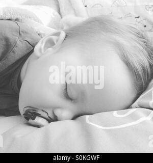 9 mese fa baby boy , dentizione, febbricitante sta prendendo un pan con il suo succhiotto sul suo letto dei genitori Foto Stock