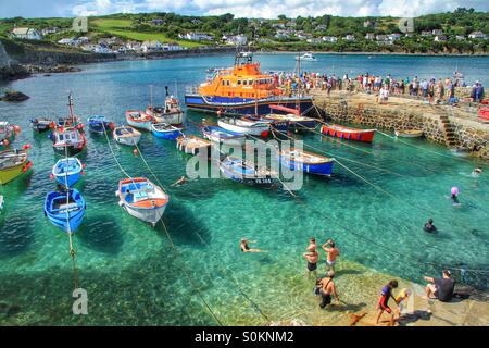 Un occupato Cornish harbour durante una famiglia giornata di divertimento con il RNLI scialuppa di salvataggio di presenze. Una vacanza scena di paesaggio con un sacco di turisti nuotare e divertirsi. Foto Stock