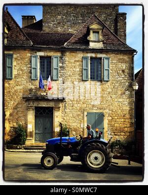 Un agricoltore guidando il trattore oltre le bandierine sul municipio di Domme rurale, Dordogne, Francia Foto Stock