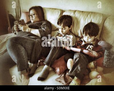 La famiglia tramite gadget sul divano. Foto Stock