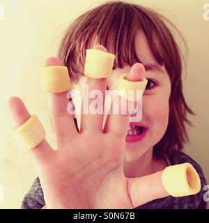 Piccolo 4 anno vecchio ragazzo con patatine sulle sue dita. Foto Stock