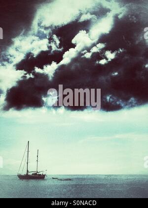 Black Storm nuvole raccolta su un singolo yacht su un oceano di calma. Foto Stock