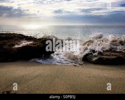 Acqua di mare impetuoso attraverso lo spazio tra due rocce su di una spiaggia di sabbia Foto Stock