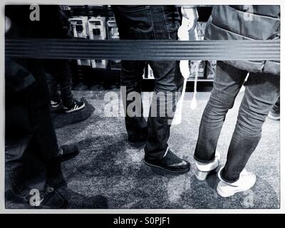 Gli amanti dello shopping in piedi in una coda dietro una barriera Foto Stock