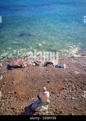 Uomo seduto sulla roccia che guarda al mare Foto Stock
