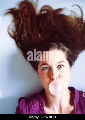 Donna con i capelli pazzo soffiando una bolla bubble gum Foto Stock