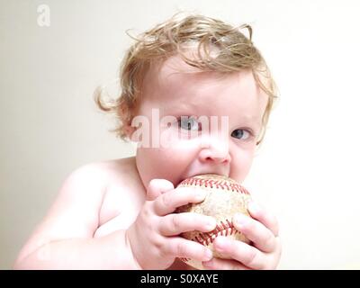 Chiave di alta immagine di un bambino masticare su un vecchio baseball Foto Stock