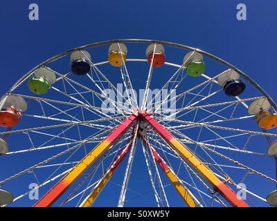 Angolo basso in prospettiva di una ruota panoramica Ferris contro un cielo blu chiaro Foto Stock