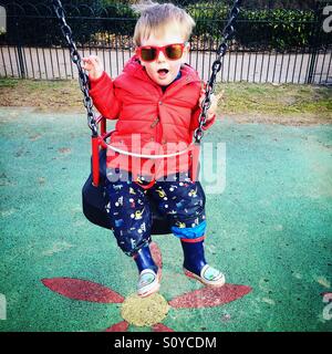 Ragazzo bambino di tire swing indossando occhiali da sole e wellies Foto Stock