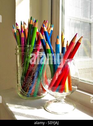 Un assortimento di matite colorate in recipienti di vetro si siede su un soleggiato davanzale Foto Stock