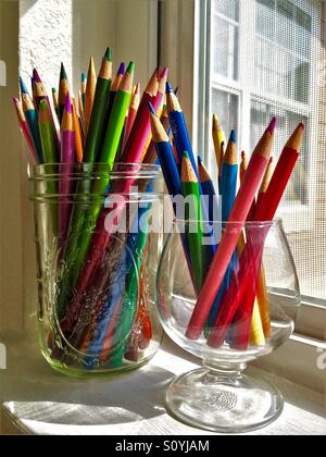Un assortimento di matite colorate sit in recipienti di vetro su un soleggiato davanzale Foto Stock