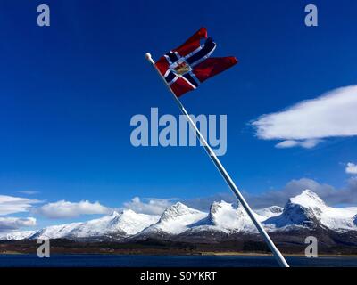 La Norwegian flag post di fronte ad una gamma di montagna. De Syv søstre (le Sette Sorelle) è una catena montuosa sull isola di Alsten in Norvegia. Foto Stock