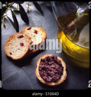 Nero-stagionati home-cured Empeltre spagnolo olive tapenade con una ampolla di olio extra vergine di oliva e biscotti. Foto Stock