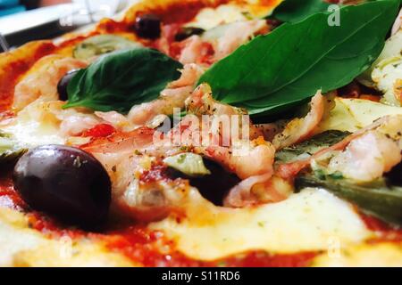 La pizza fatta in casa. Pancetta, carciofi, olive e mozzarella su una base di pomodoro, guarnito con basilico fresco. Foto Stock
