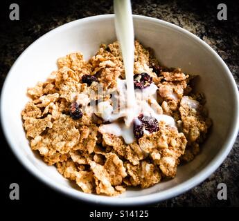 Versare il latte in una ciotola con fiocchi di cereali e frutta secca. Foto Stock