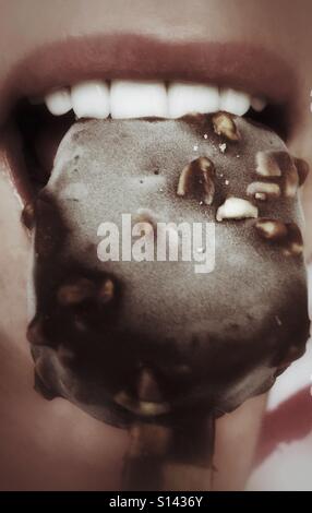Un primo piano di denti mordere in un cioccolato-coperti gelati su un bastone. Foto Stock