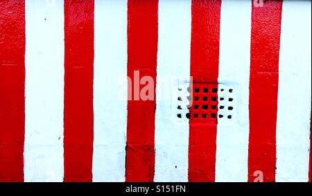 Strisce rosse e bianche dipinta su un muro di mattoni di ventilazione Foto Stock