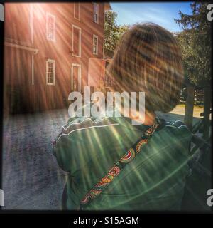 Una signora di scattare una foto di un edificio rosso con un Iphone. Il sole crea prisma-come raggi attraverso la scena. Foto Stock