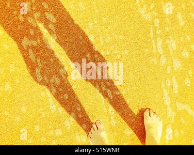 Donna di piedi e la sua ombra mentre wading presso la spiaggia. Foto Stock