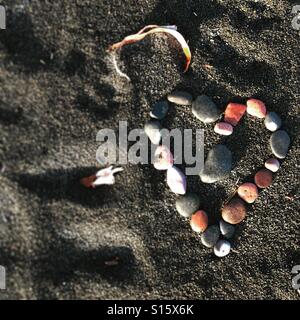 Pietre a forma di cuore sulla spiaggia di sabbia nera Foto Stock