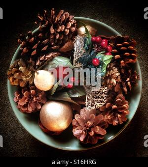 Guardando verso il basso su una ciotola di festosa, inverno decorazioni, con frutti di bosco, coni e foglie Foto Stock