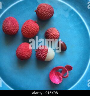 Intero e lychee pelati su una piastra di colore blu Foto Stock