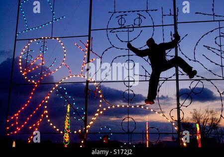 Un uomo si arrampica su un quadro di ottenere decorazioni di Natale accese per le vacanze Foto Stock