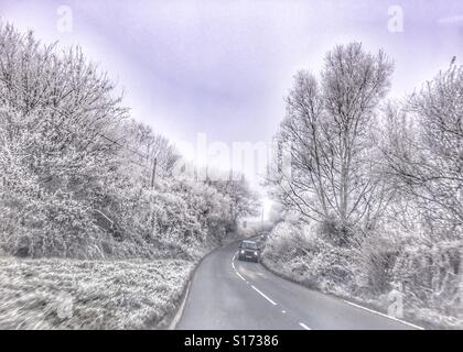 Vista del conducente attraverso il parabrezza per la strada in inverno. Il ghiaccio e la brina e avvicinando i fari anteriori delle autovetture provenienti giù per la collina. Meno 6 gradi. Foto Stock