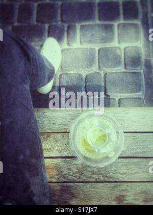 Persona con limonata in una tazza di plastica su un banco di lavoro Foto Stock