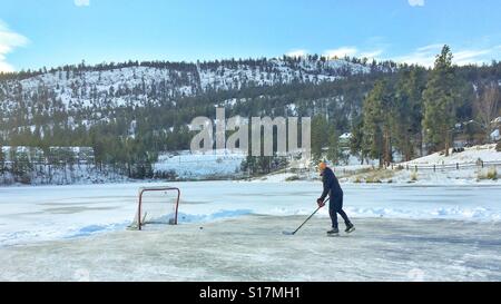 Ragazzo adolescente giocare ad hockey su un laghetto congelato in una fredda giornata invernale. Foto Stock