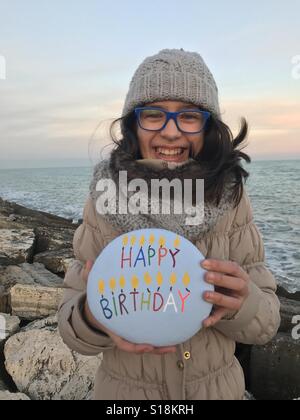 Giovane ragazza con una pietra con buon compleanno intagliati e messaggio colorato Foto Stock