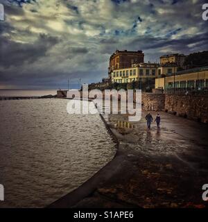 Un giovane camminando sul marciapiede attorno al lago marino in Weston super Mare, North Somerset, Inghilterra Foto Stock