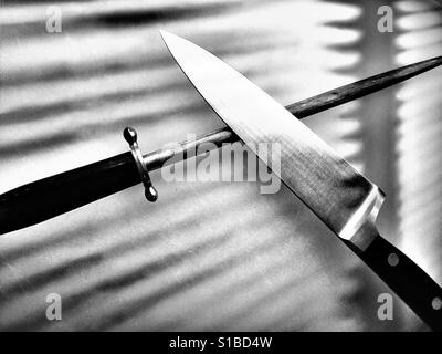 Grande coltello da cucina e affilatura di acciaio sul bancone cucina in bianco e nero Foto Stock